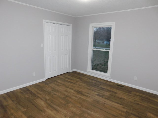 empty room featuring visible vents, baseboards, dark wood-style floors, and crown molding