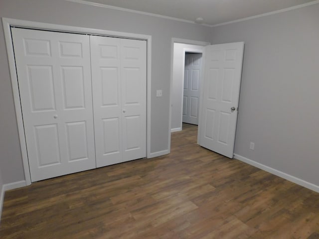 unfurnished bedroom with a closet, crown molding, baseboards, and dark wood-style flooring