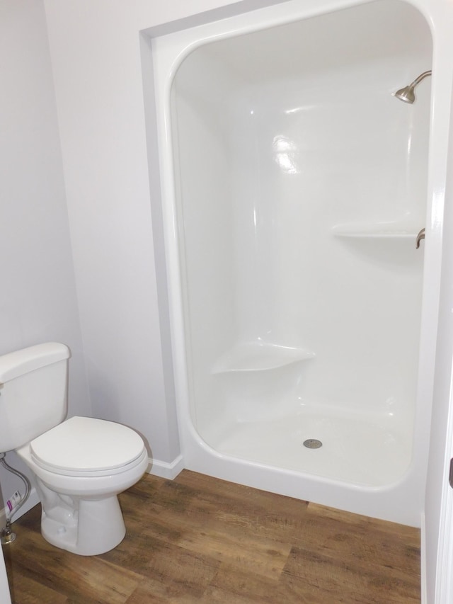 bathroom with a walk in shower, toilet, baseboards, and wood finished floors