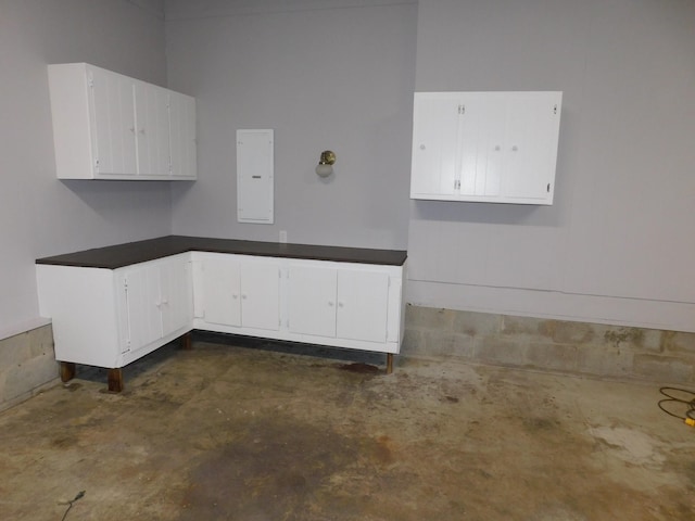 kitchen with electric panel, dark countertops, unfinished concrete floors, and white cabinetry