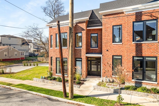 view of property featuring brick siding, a shingled roof, and a residential view