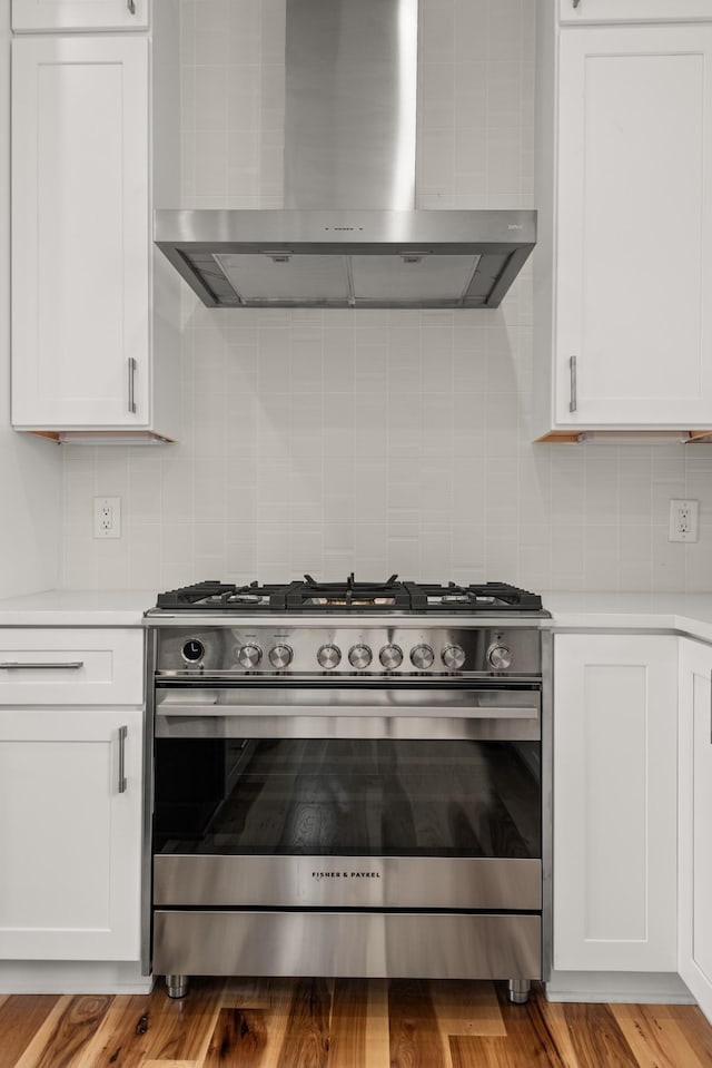 kitchen with light countertops, decorative backsplash, white cabinets, wall chimney range hood, and high end stove