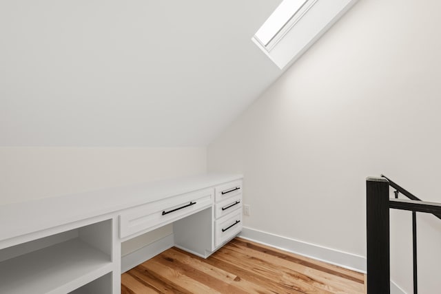 unfurnished office featuring vaulted ceiling with skylight, light wood-style flooring, and baseboards