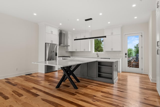 kitchen with wall chimney range hood, a large island, white cabinets, and stainless steel fridge with ice dispenser