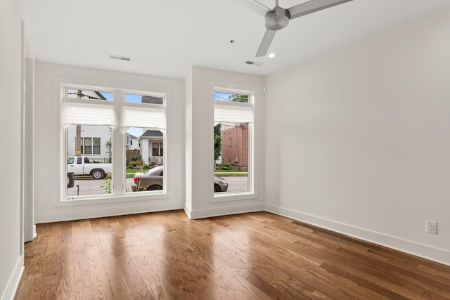 unfurnished room with ceiling fan, wood finished floors, visible vents, and baseboards