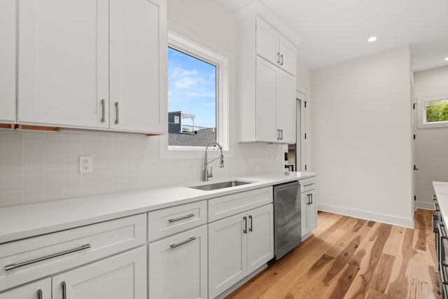 kitchen with white cabinets, light wood-style flooring, a sink, light countertops, and backsplash