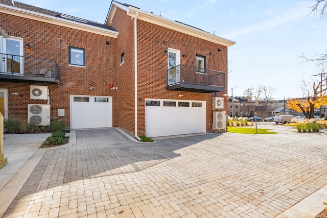 exterior space featuring decorative driveway, brick siding, a balcony, and an attached garage