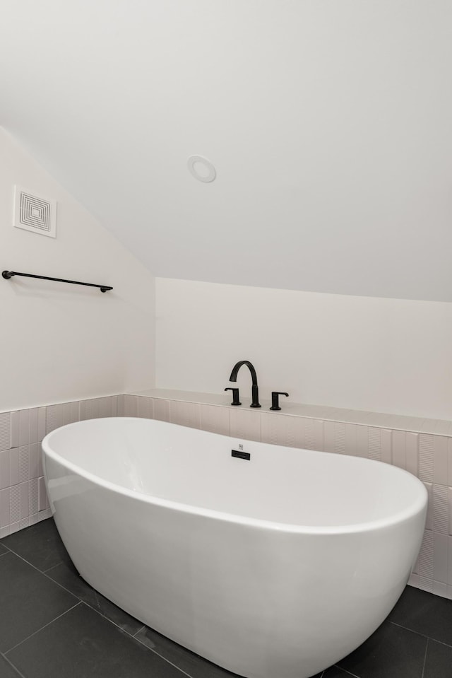 full bathroom with lofted ceiling, a freestanding tub, tile walls, and tile patterned floors