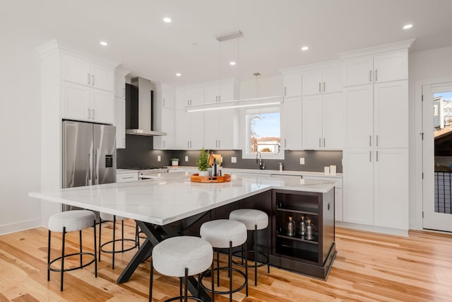 kitchen featuring light wood-style flooring, white cabinets, wall chimney range hood, a large island, and tasteful backsplash