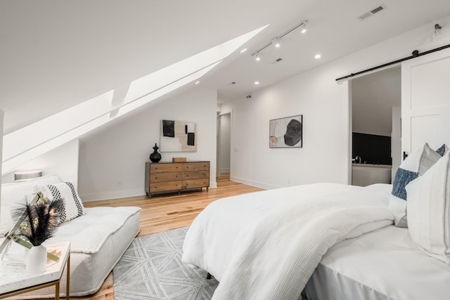 bedroom with a barn door, visible vents, baseboards, lofted ceiling with skylight, and light wood-type flooring