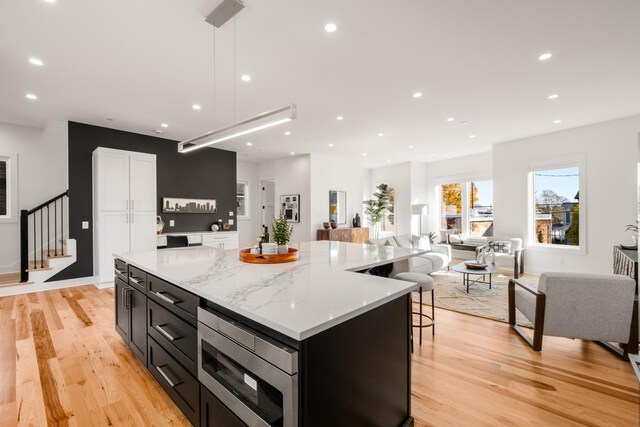 kitchen featuring a spacious island, stainless steel microwave, light wood-style flooring, and dark cabinetry