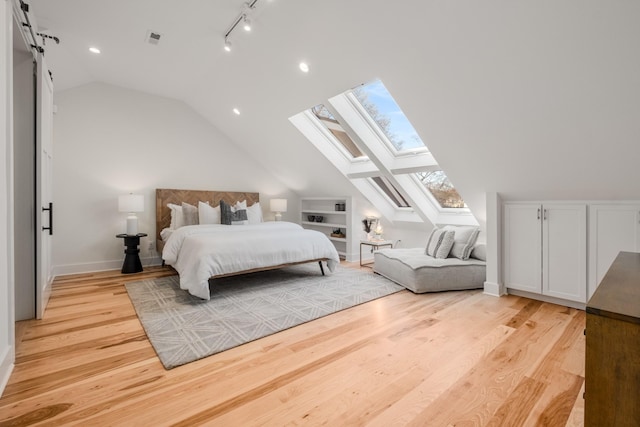 bedroom with visible vents, vaulted ceiling with skylight, a barn door, and light wood-style flooring