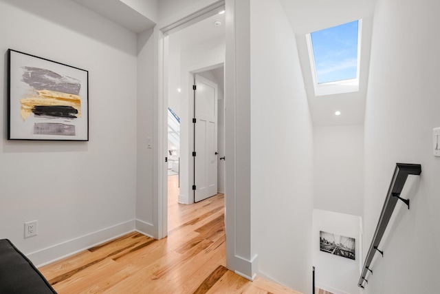 corridor featuring light wood finished floors, a skylight, baseboards, and an upstairs landing