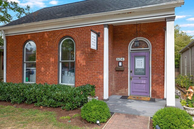 view of exterior entry featuring a shingled roof and brick siding