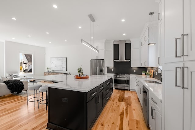 kitchen featuring a center island, stainless steel appliances, a sink, dark cabinetry, and wall chimney exhaust hood