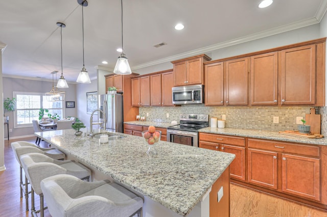 kitchen featuring a kitchen island with sink, stainless steel appliances, visible vents, brown cabinets, and light wood finished floors