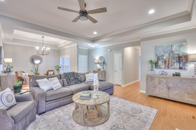 living room with light wood finished floors, a tray ceiling, ceiling fan with notable chandelier, and recessed lighting