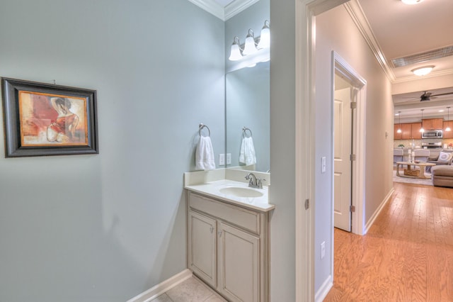 bathroom featuring wood finished floors, vanity, visible vents, baseboards, and ornamental molding