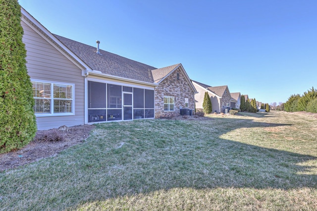 rear view of property with roof with shingles, a lawn, and a sunroom