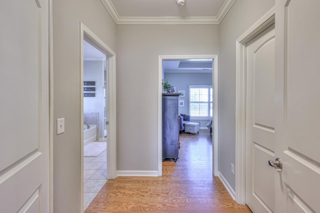 corridor featuring ornamental molding, baseboards, and light wood finished floors