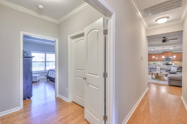 hall with light wood finished floors, baseboards, visible vents, and crown molding