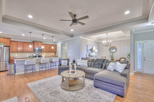 living area with baseboards, light wood-style flooring, a tray ceiling, ceiling fan with notable chandelier, and recessed lighting