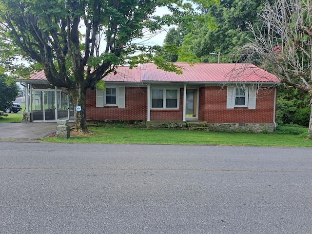 single story home with aphalt driveway, brick siding, a front yard, a sunroom, and metal roof