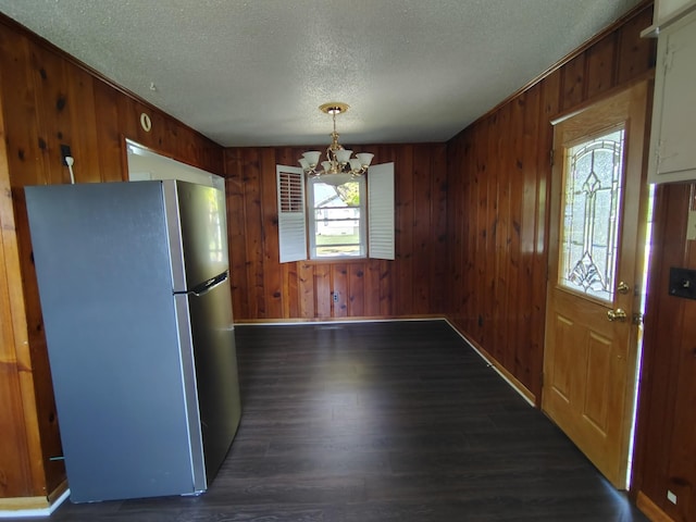 kitchen with freestanding refrigerator, dark wood-style flooring, wood walls, and an inviting chandelier