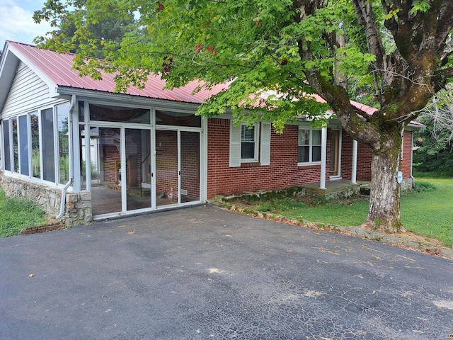 view of front facade featuring a sunroom, metal roof, and brick siding