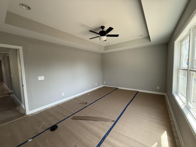 empty room featuring ceiling fan, a raised ceiling, and baseboards