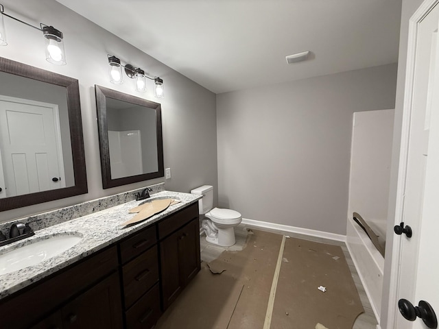 bathroom with baseboards, a sink, toilet, and double vanity