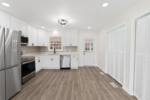 kitchen featuring stainless steel appliances, a sink, light countertops, light wood-type flooring, and backsplash