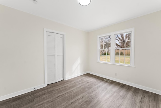 unfurnished bedroom featuring a closet, visible vents, dark wood finished floors, and baseboards