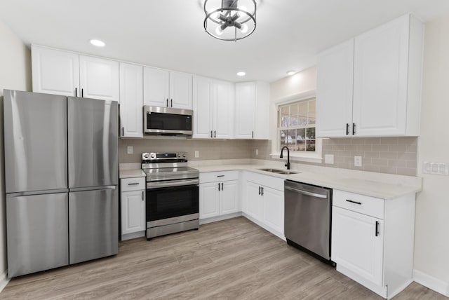 kitchen with appliances with stainless steel finishes, backsplash, a sink, and light wood-style flooring