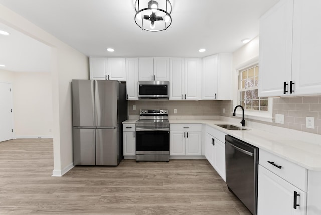 kitchen with a sink, white cabinets, light wood-style floors, appliances with stainless steel finishes, and decorative backsplash