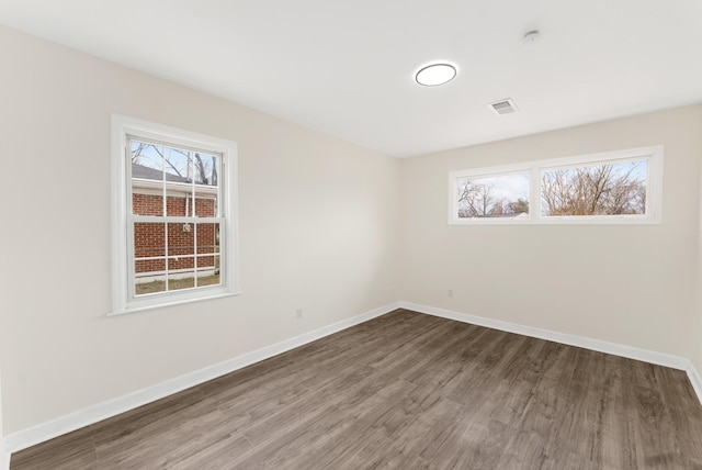 spare room featuring wood finished floors, visible vents, and baseboards