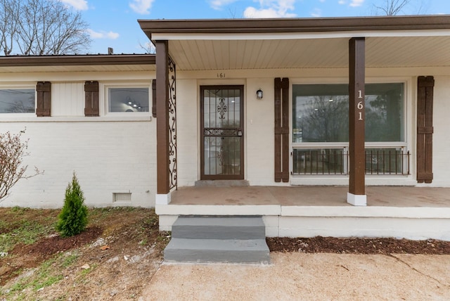 view of exterior entry featuring brick siding, crawl space, and a porch