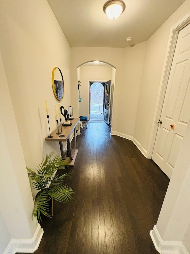 corridor featuring dark wood-style floors, arched walkways, and baseboards