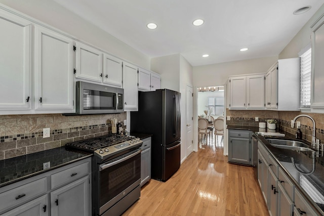 kitchen featuring light wood finished floors, appliances with stainless steel finishes, white cabinets, a sink, and dark stone counters