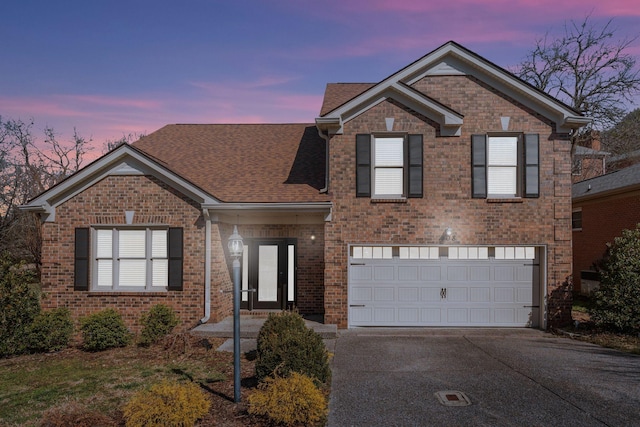 traditional-style house with driveway, roof with shingles, an attached garage, and brick siding