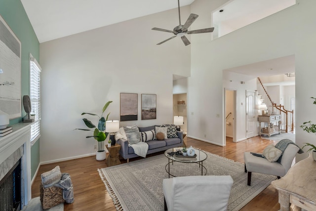 living room featuring a tile fireplace, wood finished floors, a ceiling fan, baseboards, and stairs