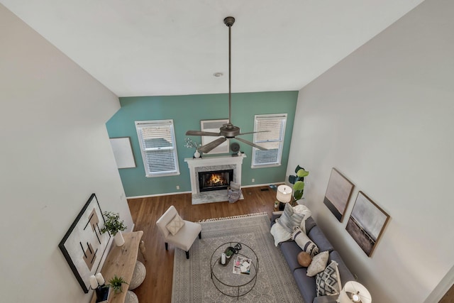 living room featuring a ceiling fan, a fireplace, baseboards, and wood finished floors