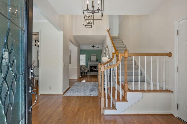 entryway with ceiling fan, wood finished floors, baseboards, a lit fireplace, and stairway