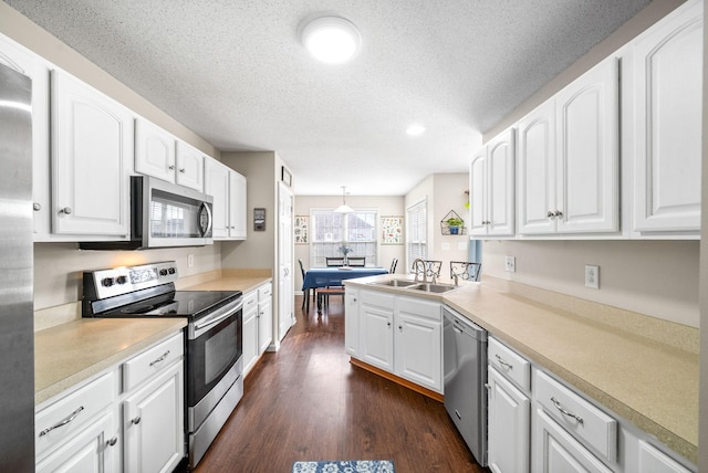 kitchen with dark wood-style flooring, a sink, white cabinetry, light countertops, and appliances with stainless steel finishes