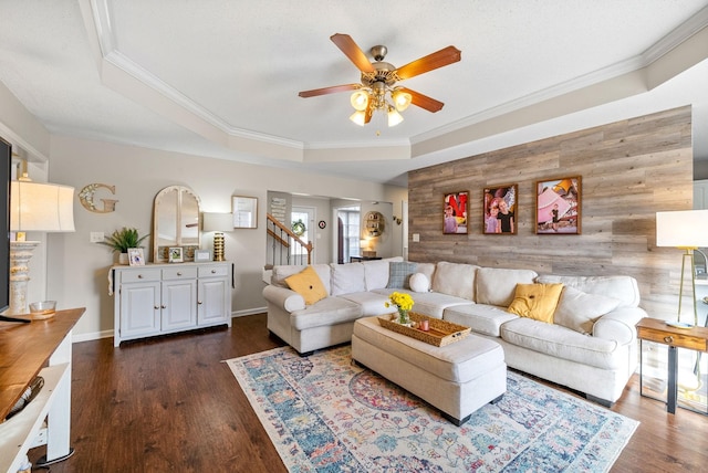 living room with stairway, a tray ceiling, dark wood finished floors, and ornamental molding