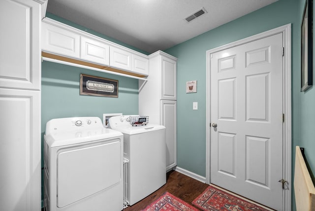 washroom with dark wood-style flooring, visible vents, cabinet space, and washer and clothes dryer