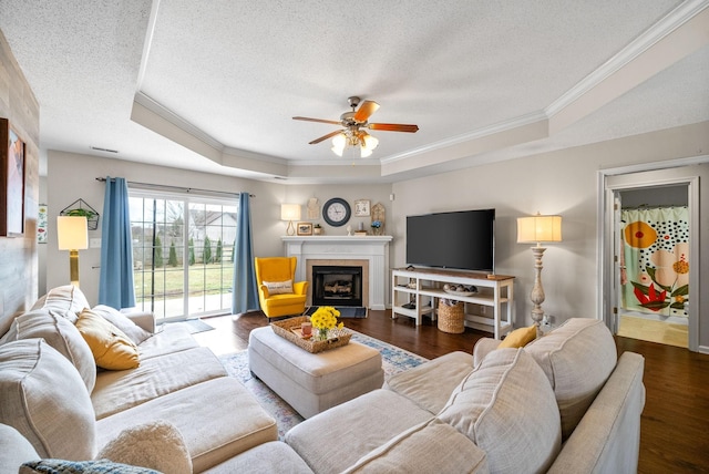 living room with a tray ceiling, crown molding, a textured ceiling, and wood finished floors