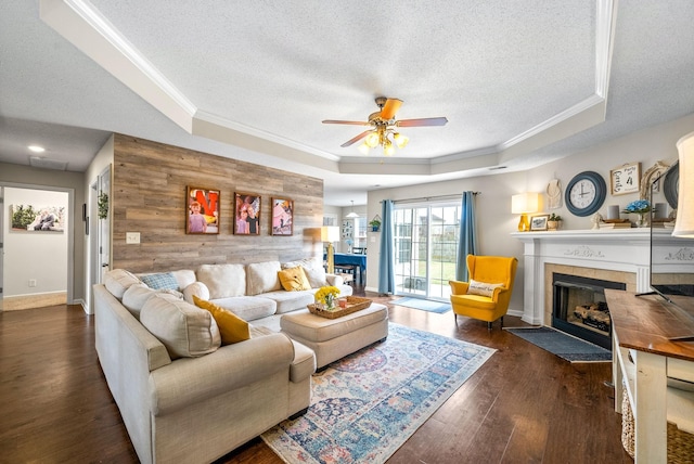 living area with a fireplace, a raised ceiling, an accent wall, wood walls, and wood finished floors