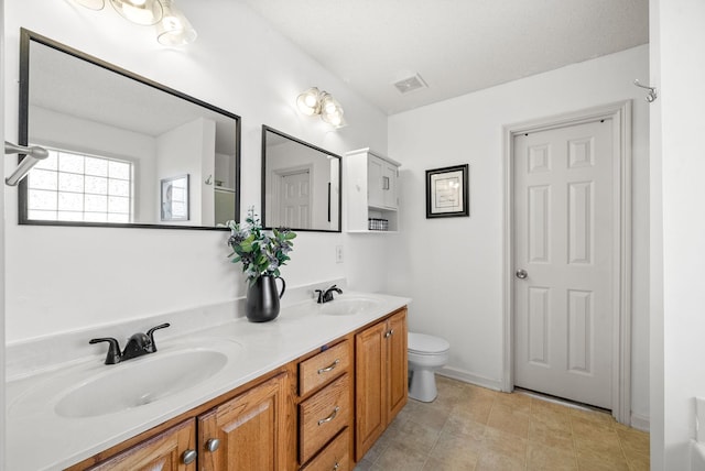 bathroom with double vanity, visible vents, toilet, and a sink