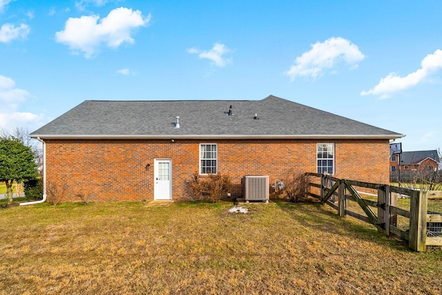 back of property featuring central AC, brick siding, fence, a yard, and roof with shingles